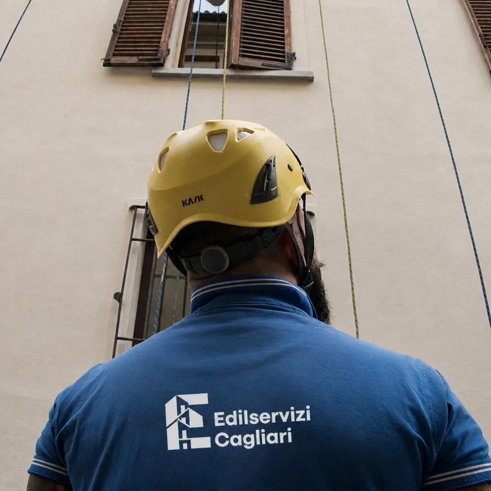 Operaio di Edilservizi Cagliari con casco e polo aziendale, di spalle davanti a una facciata in lavorazione